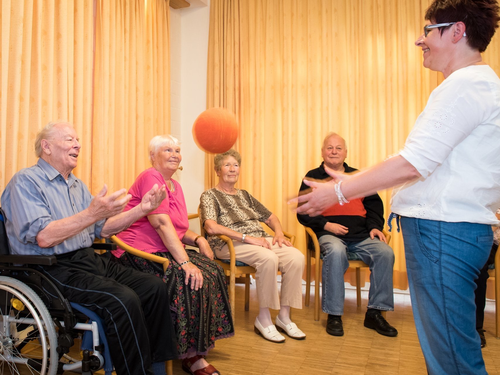 Koordinationsübung: eine gemschte Gruppe Bewohner spielen Ball mit einer Pflegerin