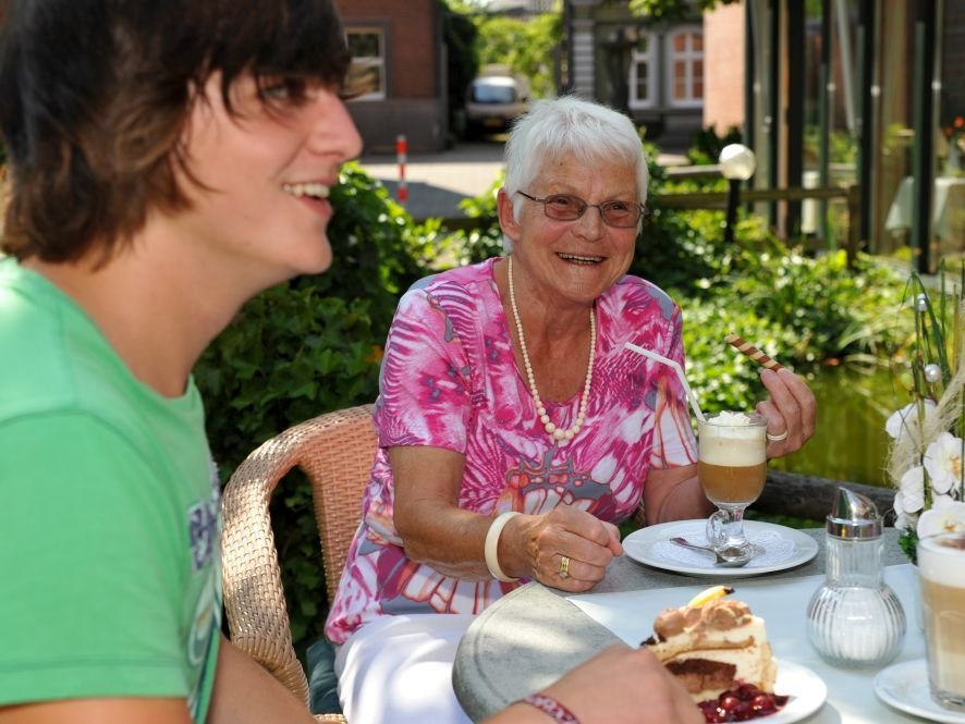 eine Frau und ein junger Mann trinken Kaffee im Garten und essen Kuchen dazu - heitere Stimmung