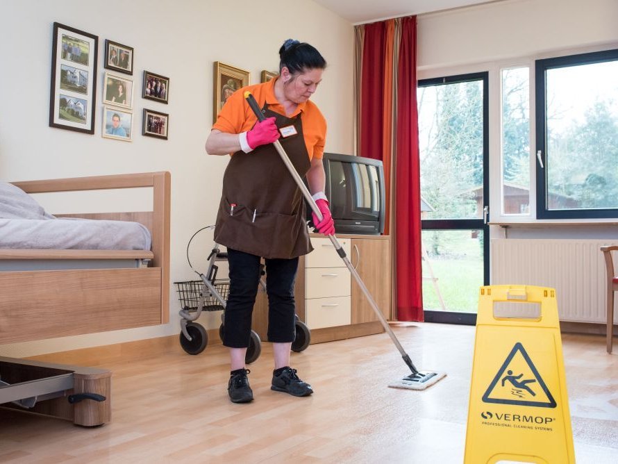 Eine weibliche Reinigungskraft wischt den Boden in einem Zimmer