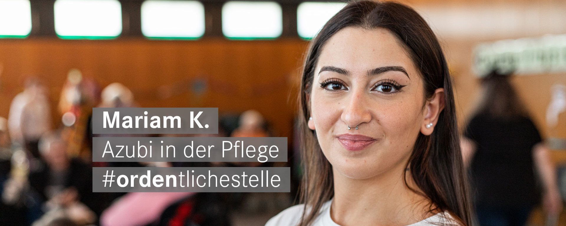 Auszubildende mit langen braunen Haaren und Nasenpiercing laechelt freundlich in die Kamera