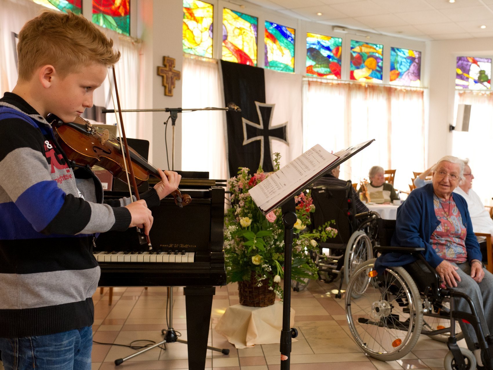Konzert im Speisesaal: ein Junge spielt Geige vor einem Notenständer - die Bewohner lauschen
