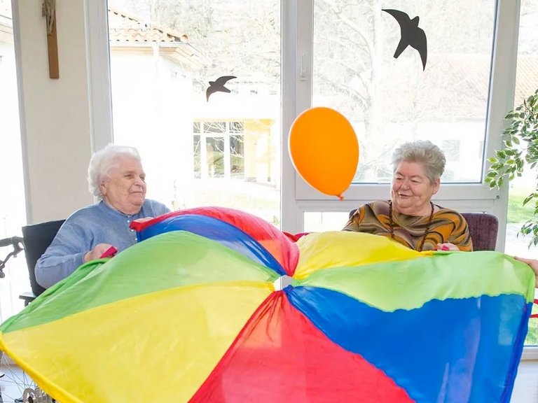 vier Frauen "balancieren" einen Luftballon mit Hilfe eines großen Tuchs, das sie gemeinsam halten
